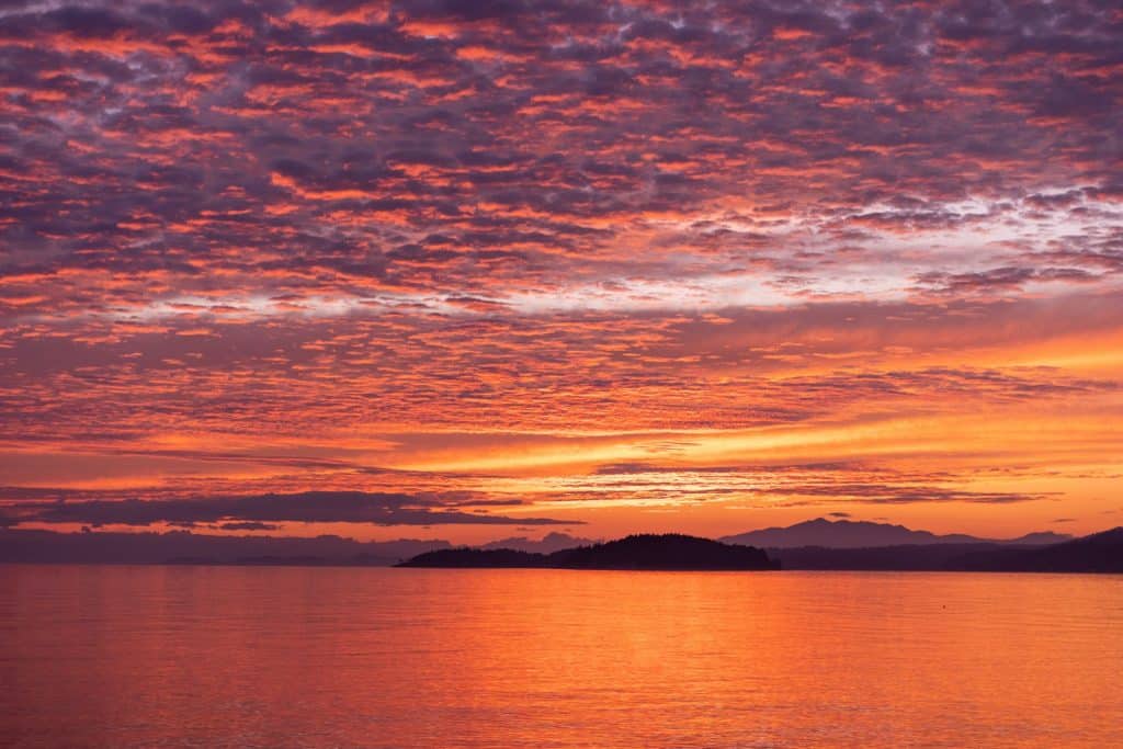 a sunset over a body of water with mountains in the background. Sunshine Coast