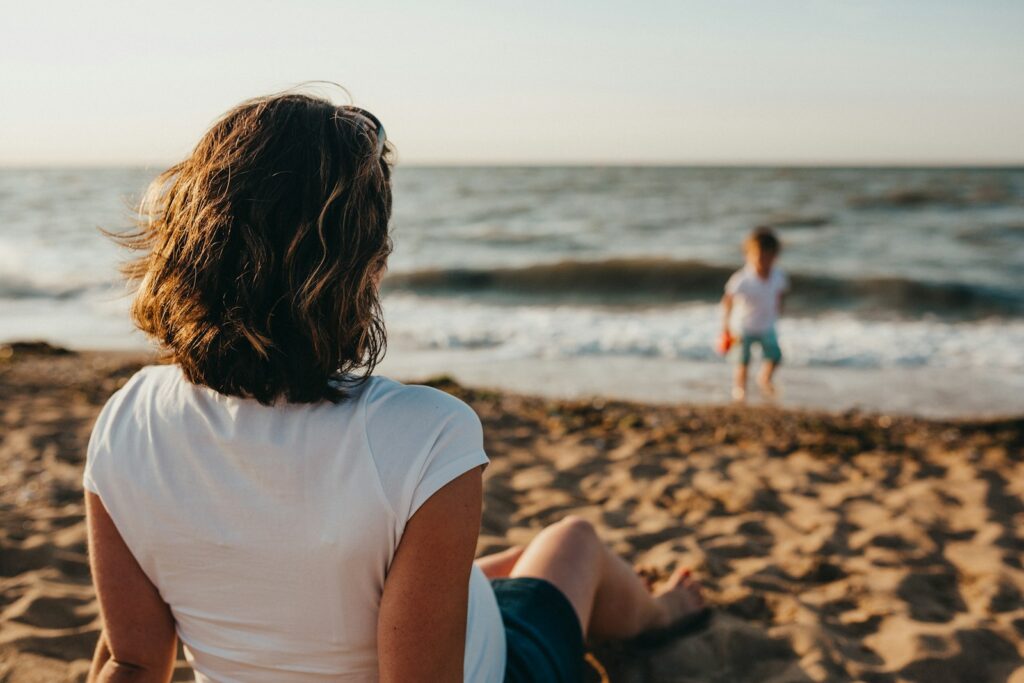 Woman watching child playing on beach. Bowen Therapy Brisbane