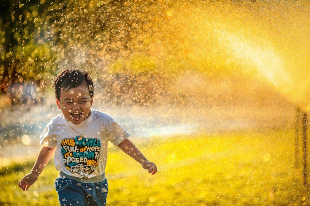 Young boy running through a sprinkler. Bowen Therapy Brisbane