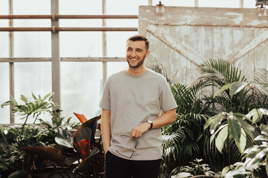 Man in grey crew-neck top holding sunglasses standing near plants. Naturopath for Men's Health