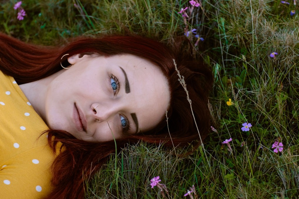 woman in brown and white polka-dot top lying in green grass. Clinical Hypnotherapist and Strategic Psychotherapist