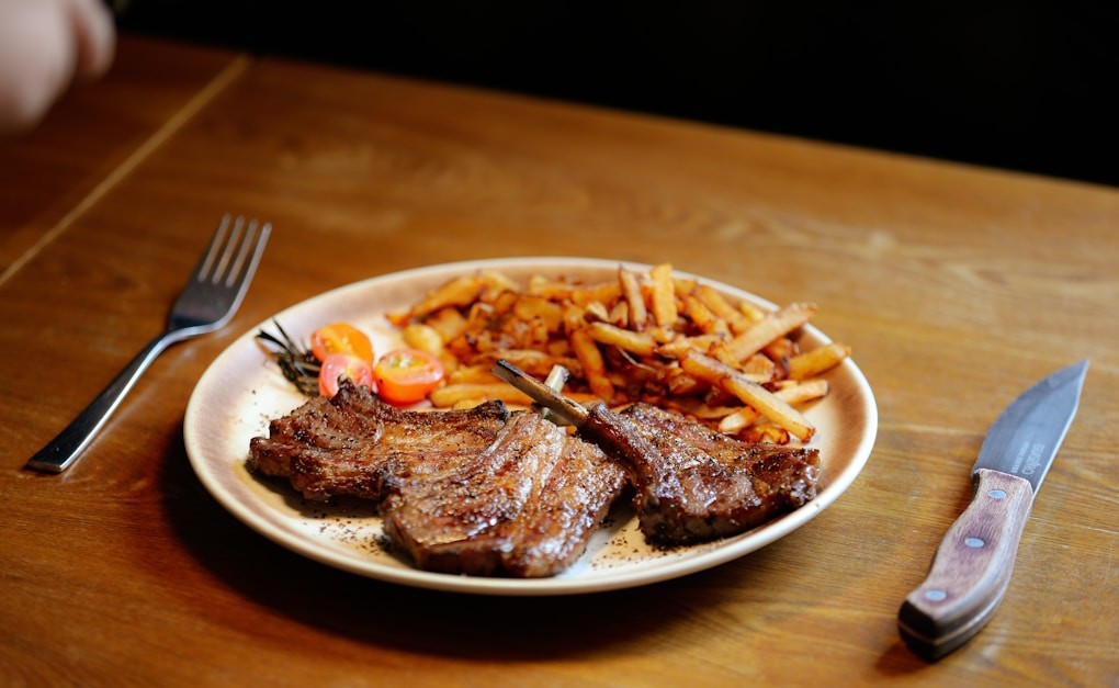 A plate of steak, french fries and a fork on a table