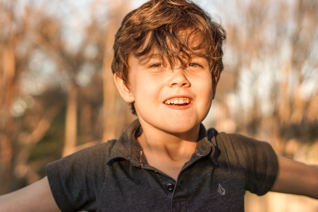 Boy in black polo shirt smiling with arms outstretched