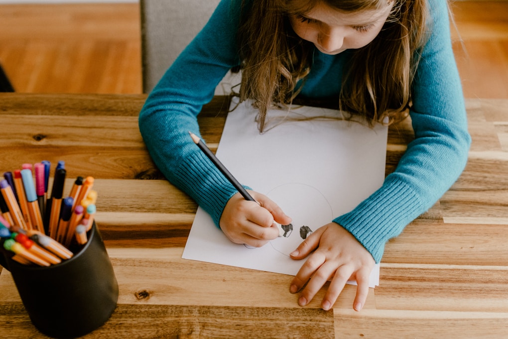 Young girl sitting at a table with colored pencils and paper