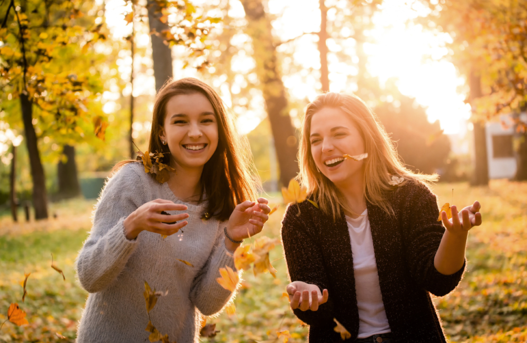 Two female friends having fun in a park filled with fallen leaves. Naturopath Cannon Hill. Brisbane Livewell Clinic